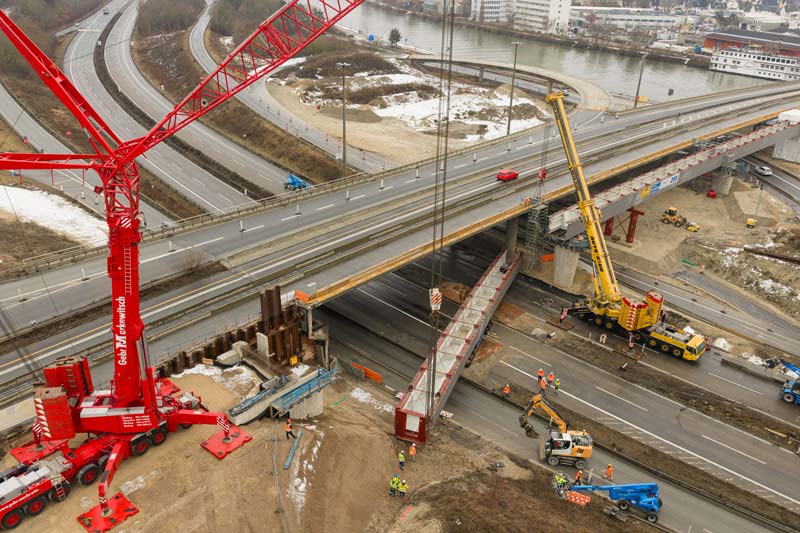 Luftaufnahme des Beginns des Brückeneinschubs der Ersatzbrücke des Frankenschnellwegs. Trübes Wetter im Winter. Einhubkräne in Rot und Gelb.