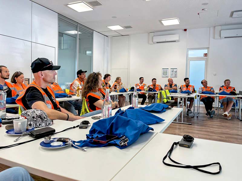 CONFIDO Ingenieure folgen aufmerksam der Präsentation: Weisse Tische, Ingenieure in Warnwesten blicken zum Vortragenden.